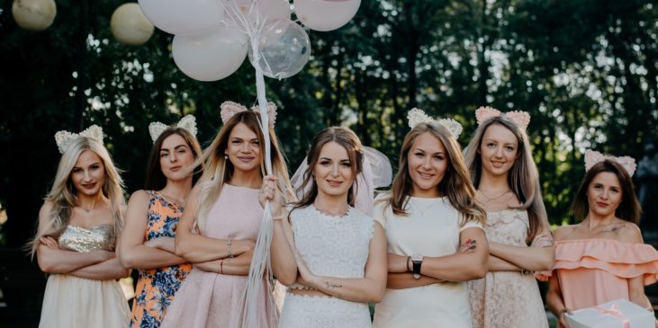 Eine Gruppe junger Frauen feiert Junggesellenabschied und hält dabei rosa Luftballons in der Hand