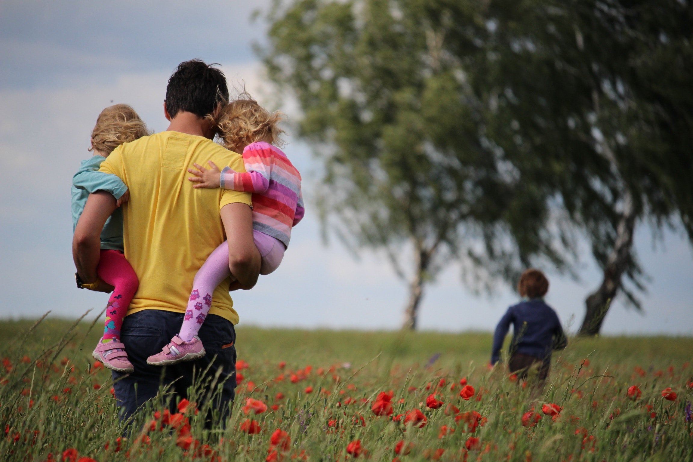 Vater trägt seine Kinder über eine Wiese mit Mohnblumen