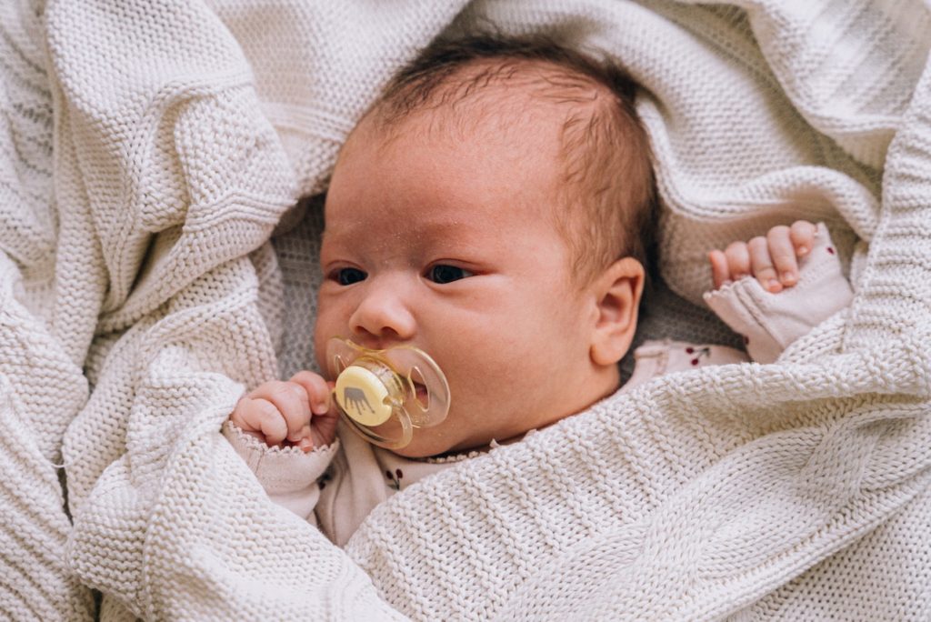 Ein Baby liegt in eine Decke eingewickelt und mit einem Schnuller im Mund