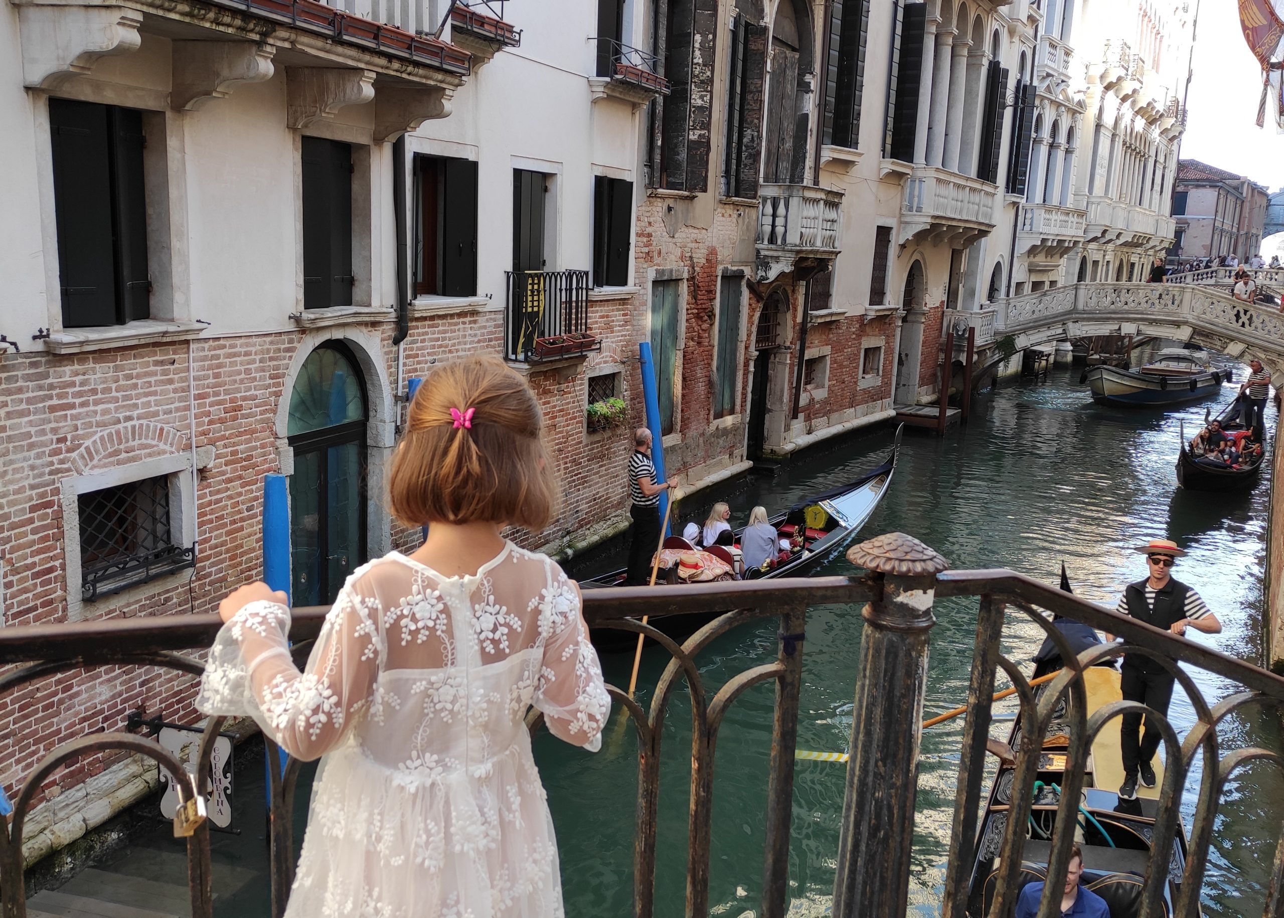 Mädchen steht auf einer Brücke in Venedig und betrachtet die Gondoliere, die Touristen durch einen kleinen Kanal fahren