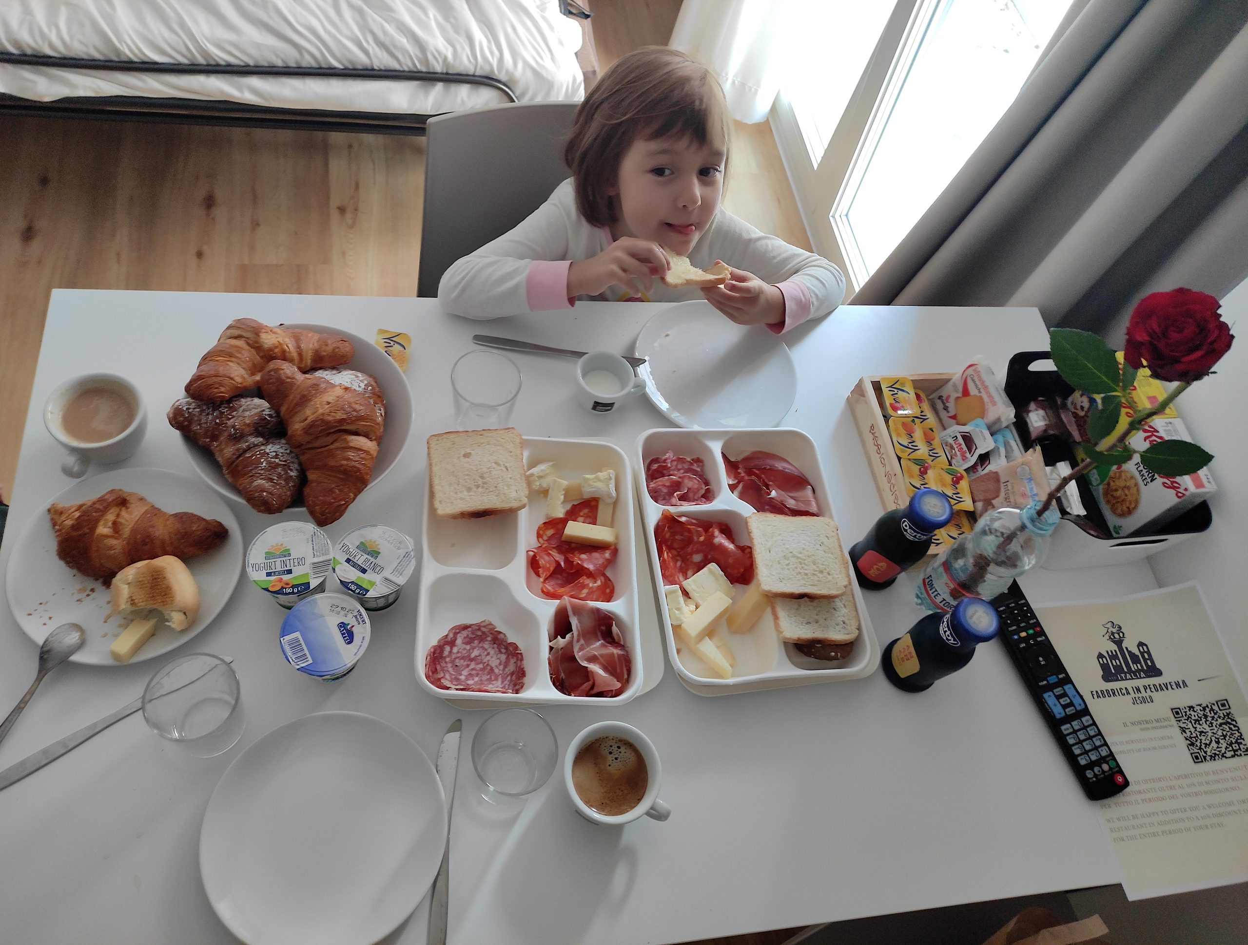Mädchen sitzt am gedeckten Frühstückstisch und isst ein Toastbrot