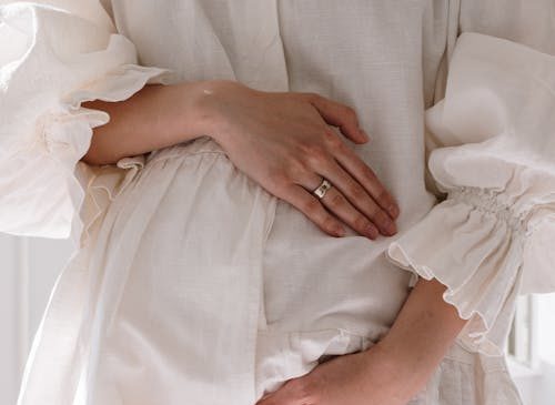 Frau in weißem Kleid hält ihren Bauch