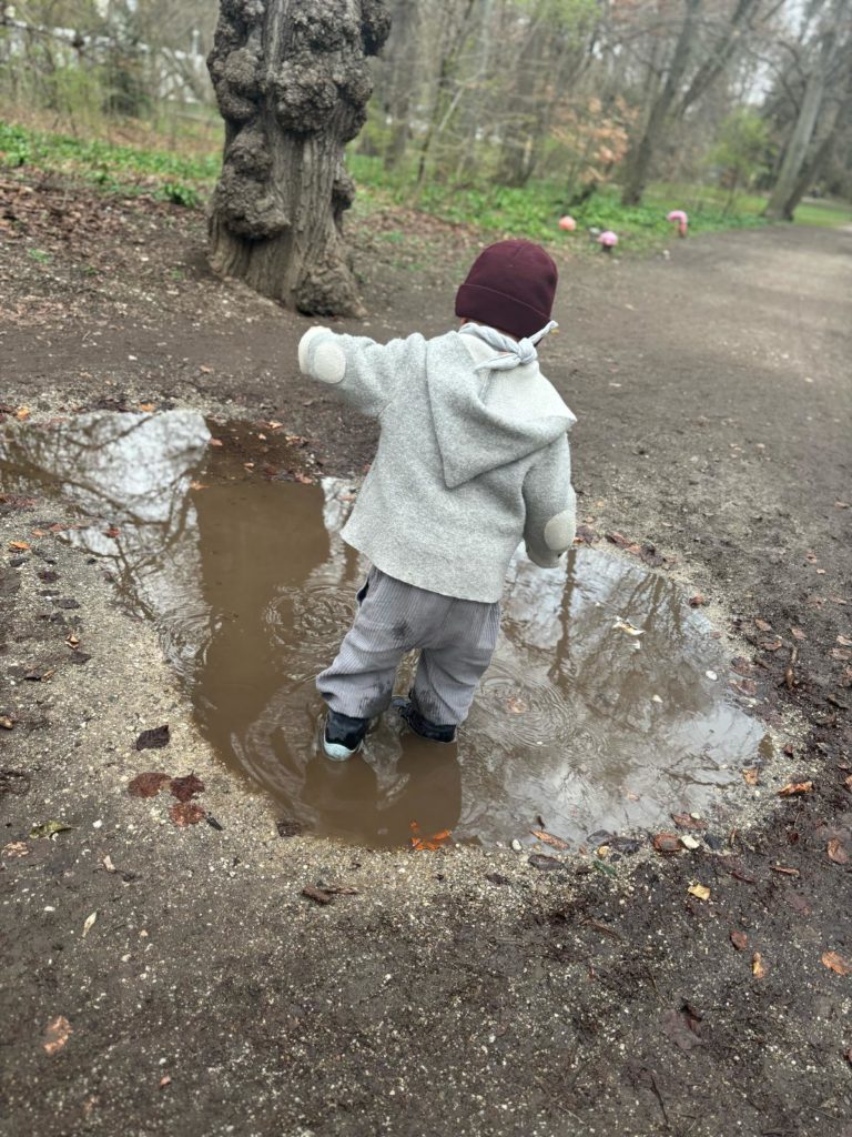 KLeinkind mit Mütze und Jacke spielt im Matsch