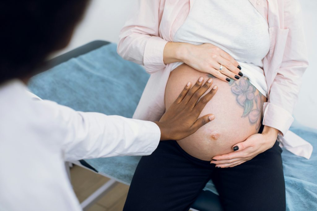 Der Bauch einer Schwangeren beim Arzt, der ihren Bauch abtastet