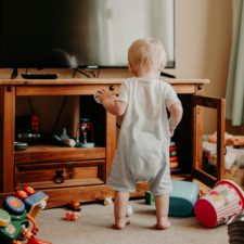 5 Dinge, die ich gern gewusst hätte, bevor ich Mama wurde Kleinkind steht im Wohnzimmer zwischen verstreutem Spielzeug – typischer Alltag mit Baby und Spielchaos
