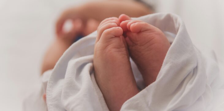 Kleine Füße und Hände eines Babys in weißem Stoff eingewickelt