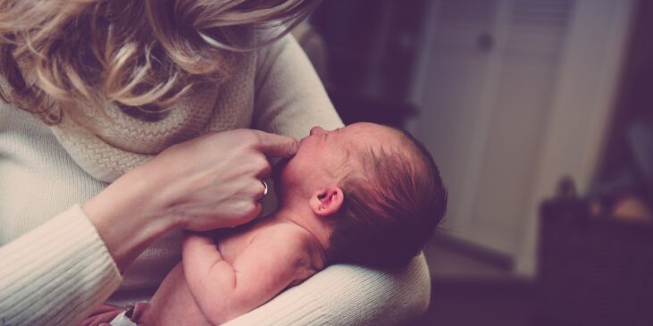 Fremdbestimmung fängt früh an: Mama hält weinendes Neugeborenes auf ihrem Arm und lässt es an ihrem Zeigefinger saugen.